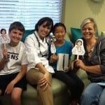 Four people seated together, smiling and holding a small drawing in a clinic waiting room