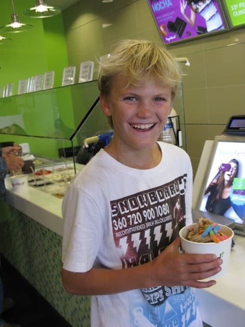 Smiling boy holding a cup of frozen yogurt inside a bright green dessert shop