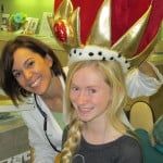 Two smiling people in costume, one wearing a gold-and-red crown-like headdress.