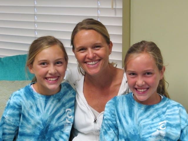 Three smiling people in blue tie-dye shirts sitting indoors on a couch