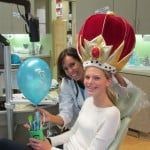 Person in a red crown-like costume sits beside a smiling person in a blue room.