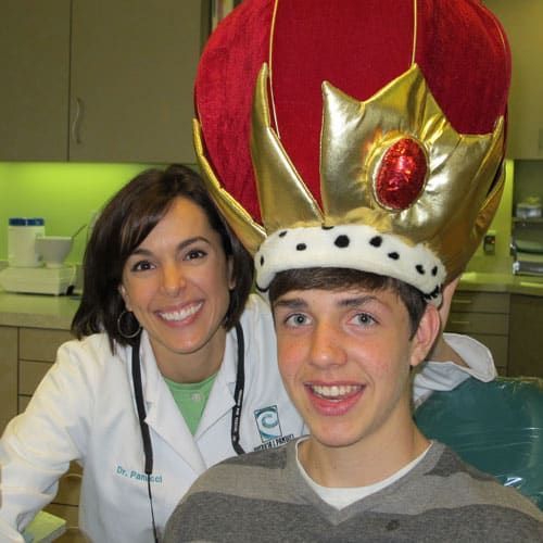 Smiling dentist and teen wearing a red-and-gold crown in a clinic