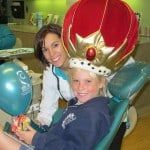 Child wearing a red crown beside a smiling woman, with blue balloons in the background