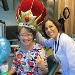 Two smiling people at a party, one wearing a red crown-like costume and the other in a light blue shirt.