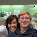 Two smiling people posing indoors in front of a green wall and shelves
