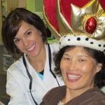 Two smiling people, one in a gold crown and red jewel, posing indoors