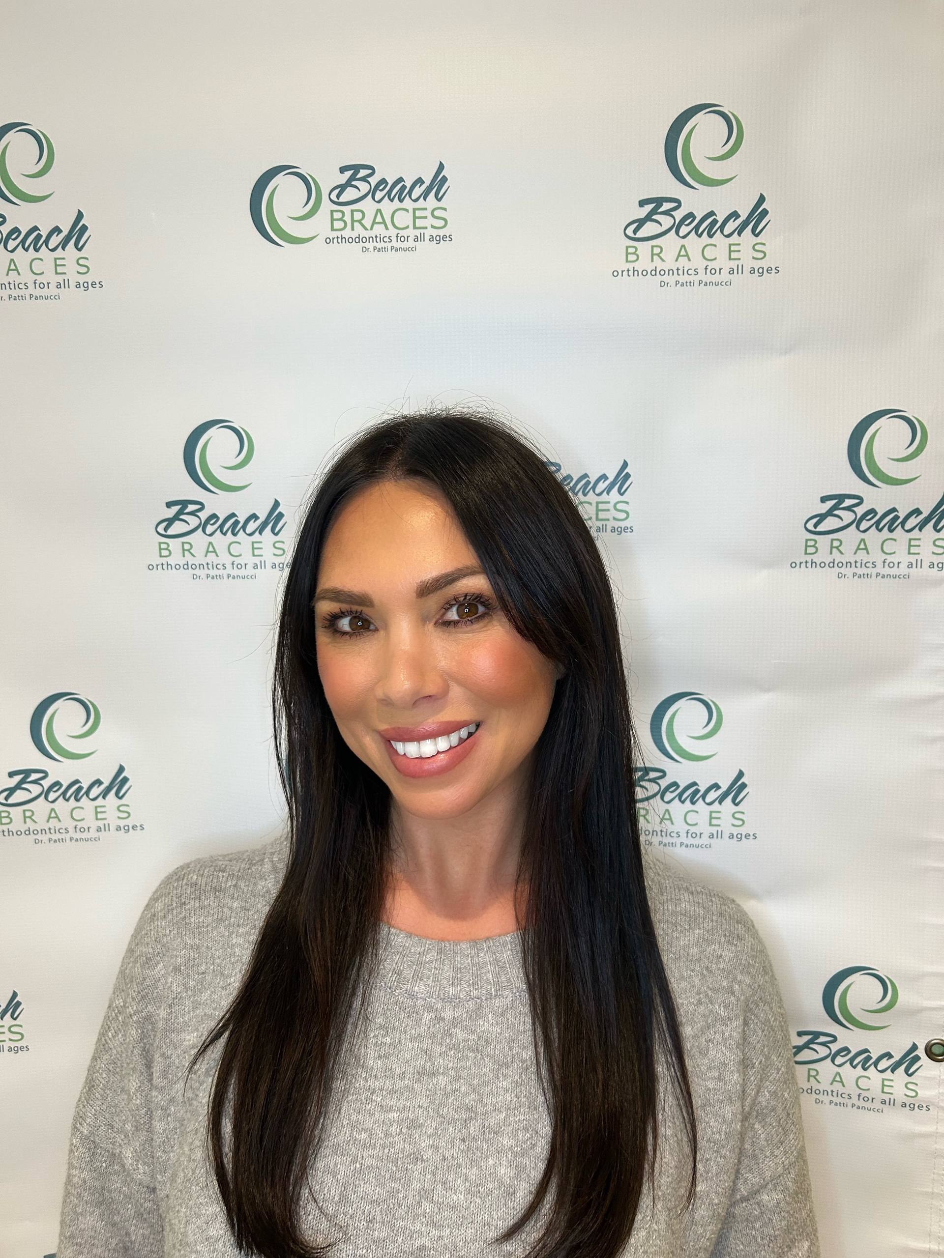 Portrait of a smiling woman with long dark hair in front of a Beach Braces logo backdrop