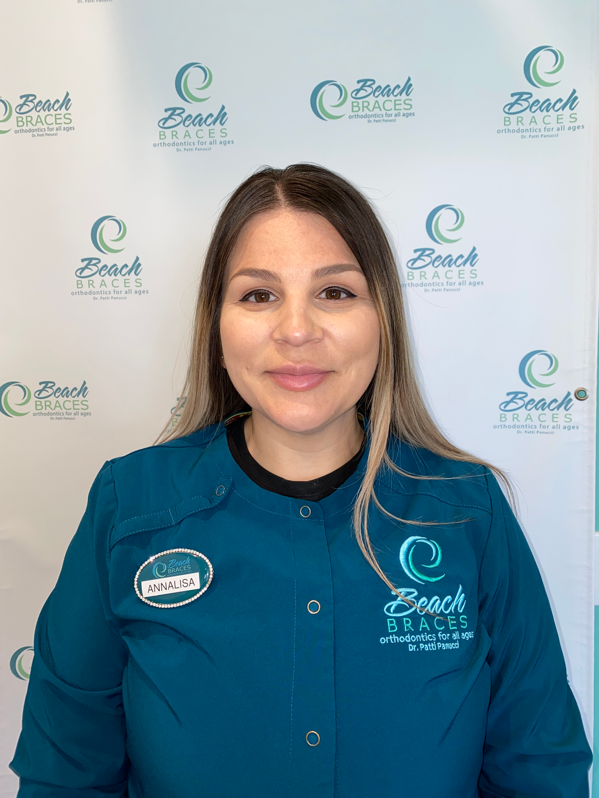 Woman in teal Beach Braces uniform smiling in front of a Beach Braces logo backdrop
