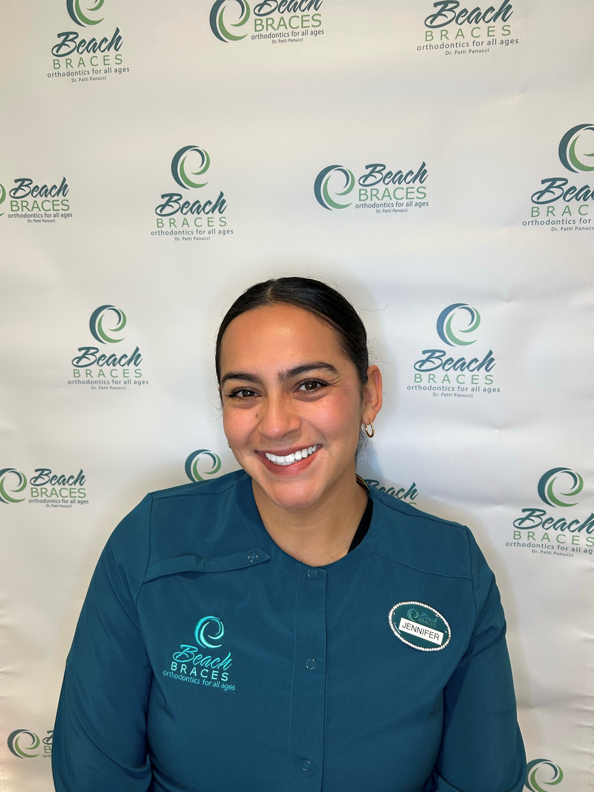 Smiling person in blue uniform standing before a branded backdrop