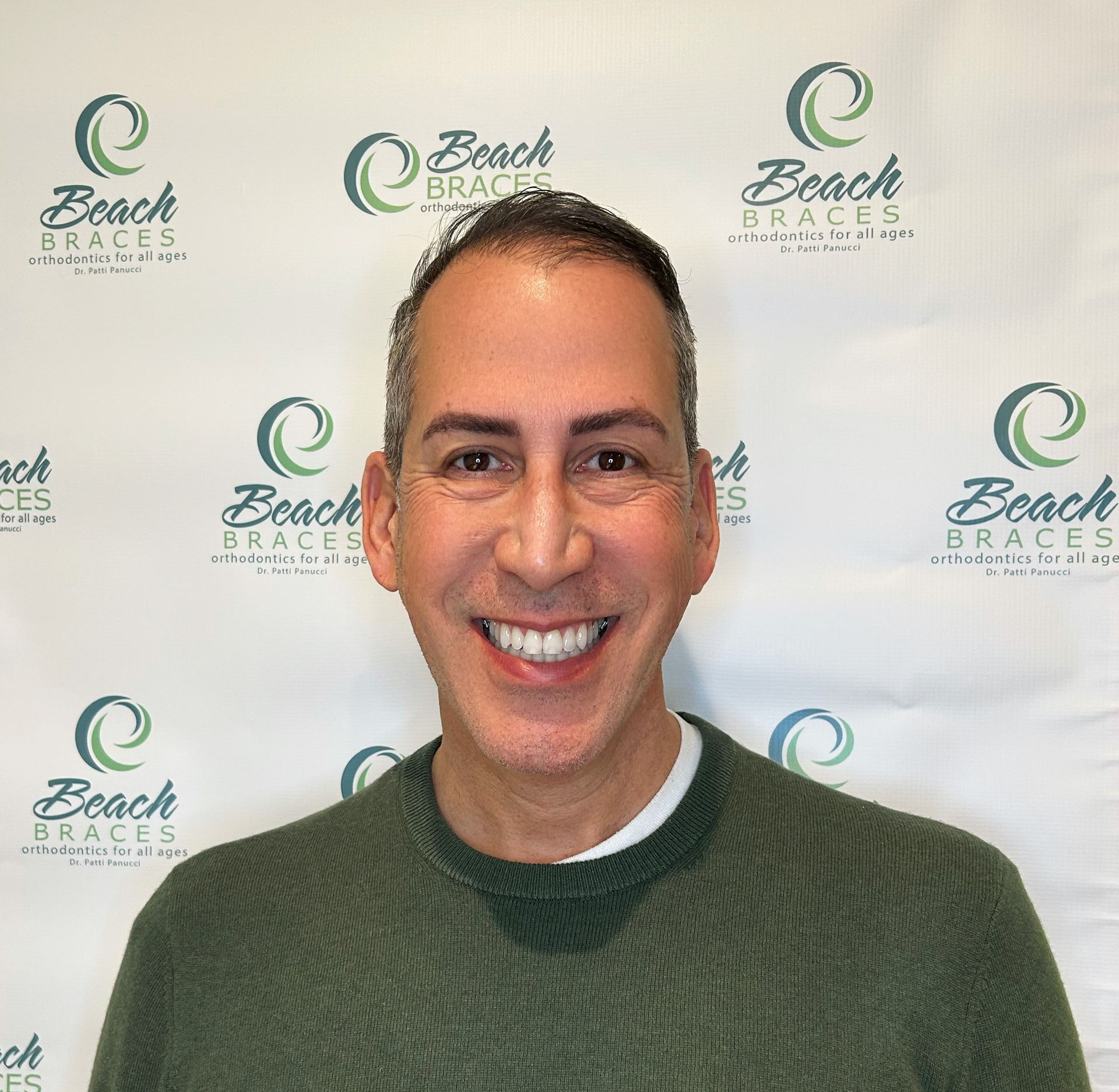 Smiling man in a green sweater standing before a Beach branding backdrop