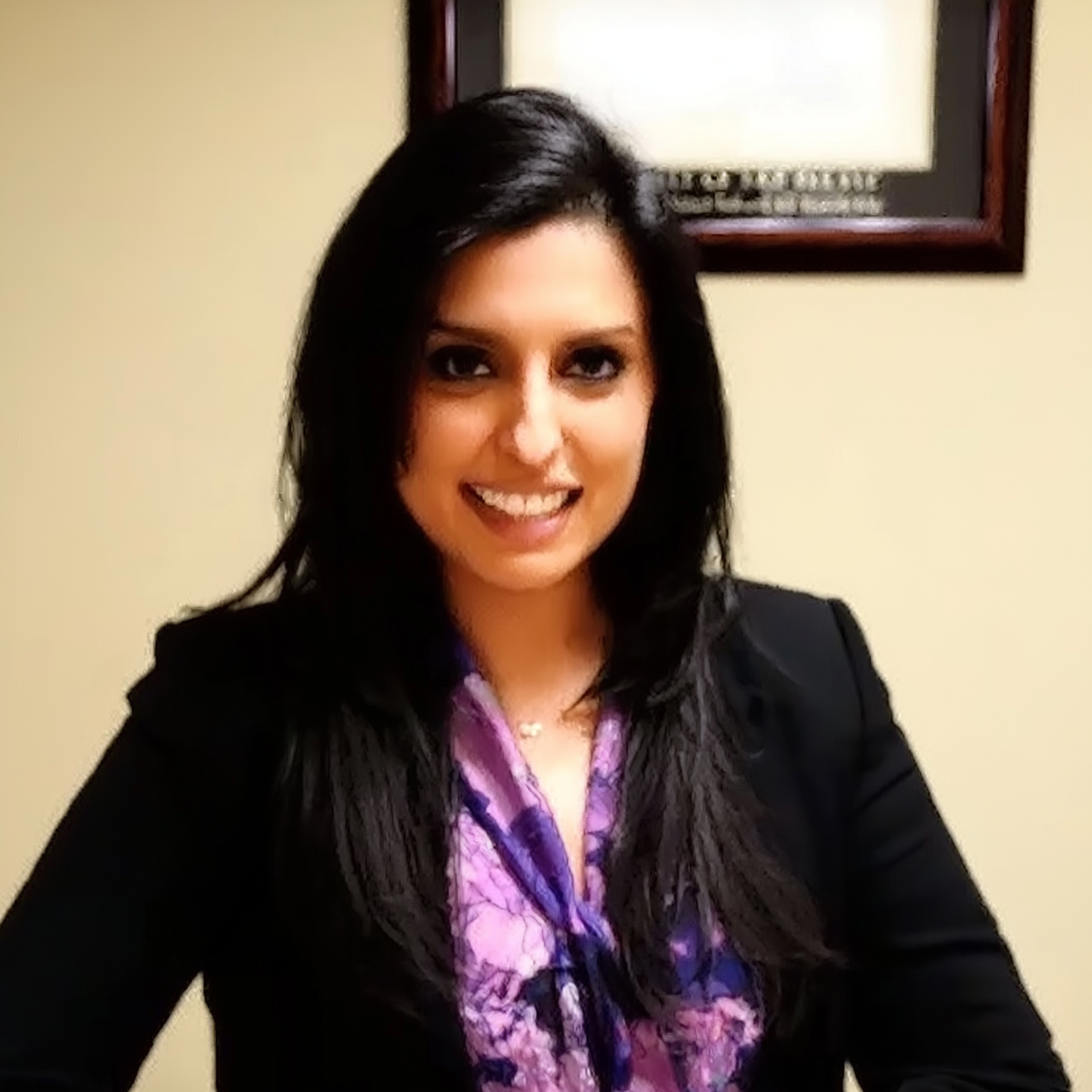 Portrait of a smiling person in a black blazer and purple blouse indoors