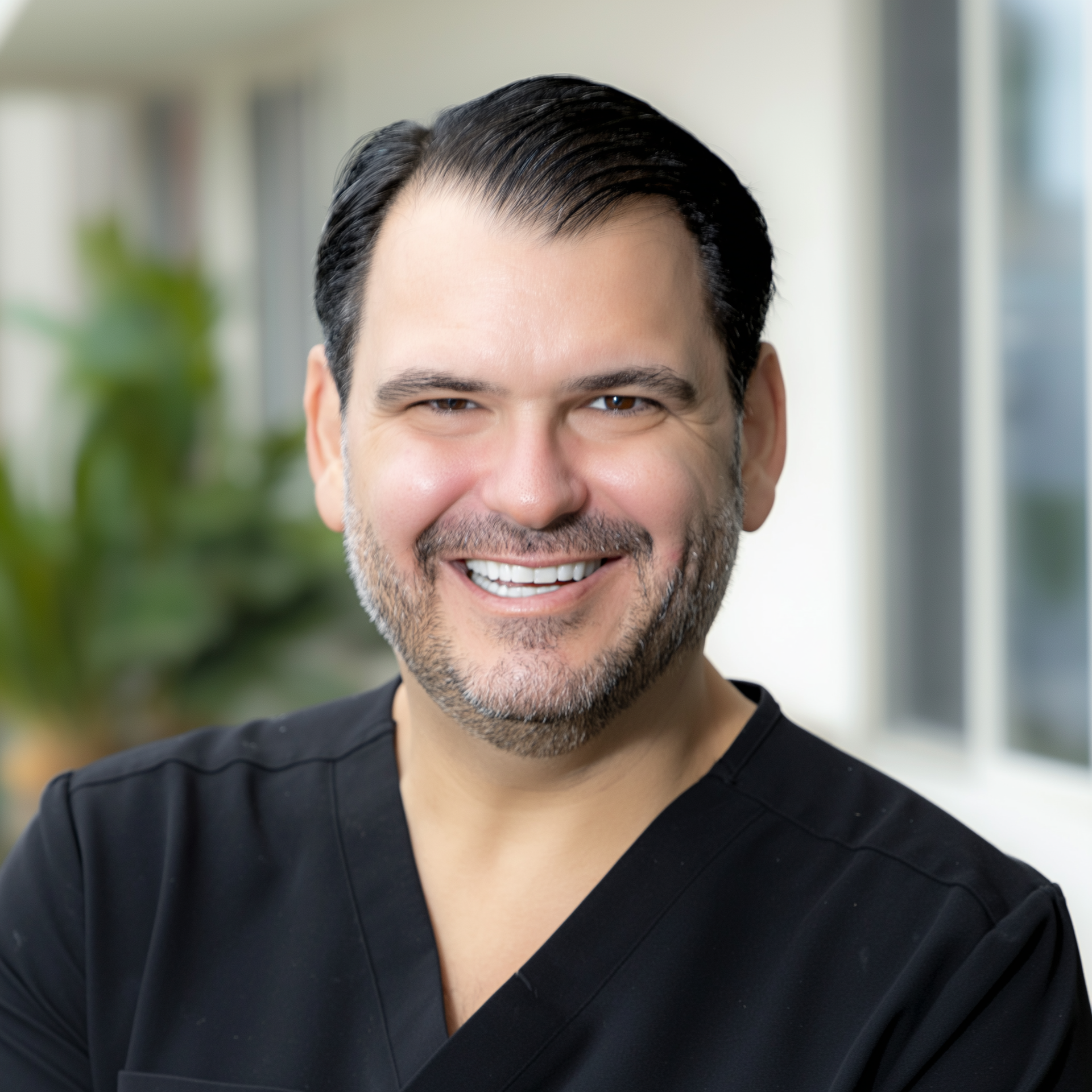 Smiling healthcare worker in black scrubs in a bright clinic hallway