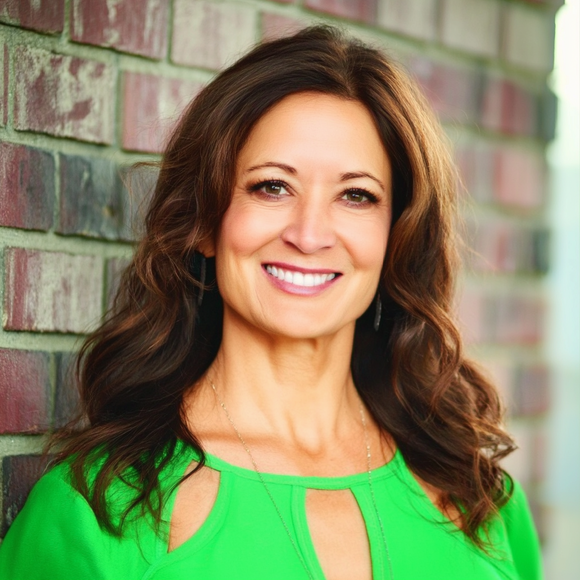 Smiling woman in a bright green top standing by a brick wall