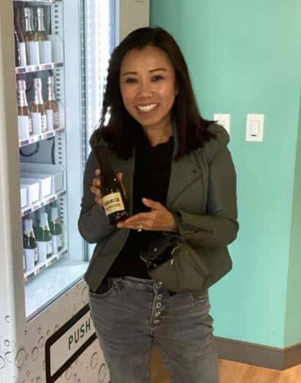 Woman holding a bottle in front of a refrigerated display, smiling in a store.