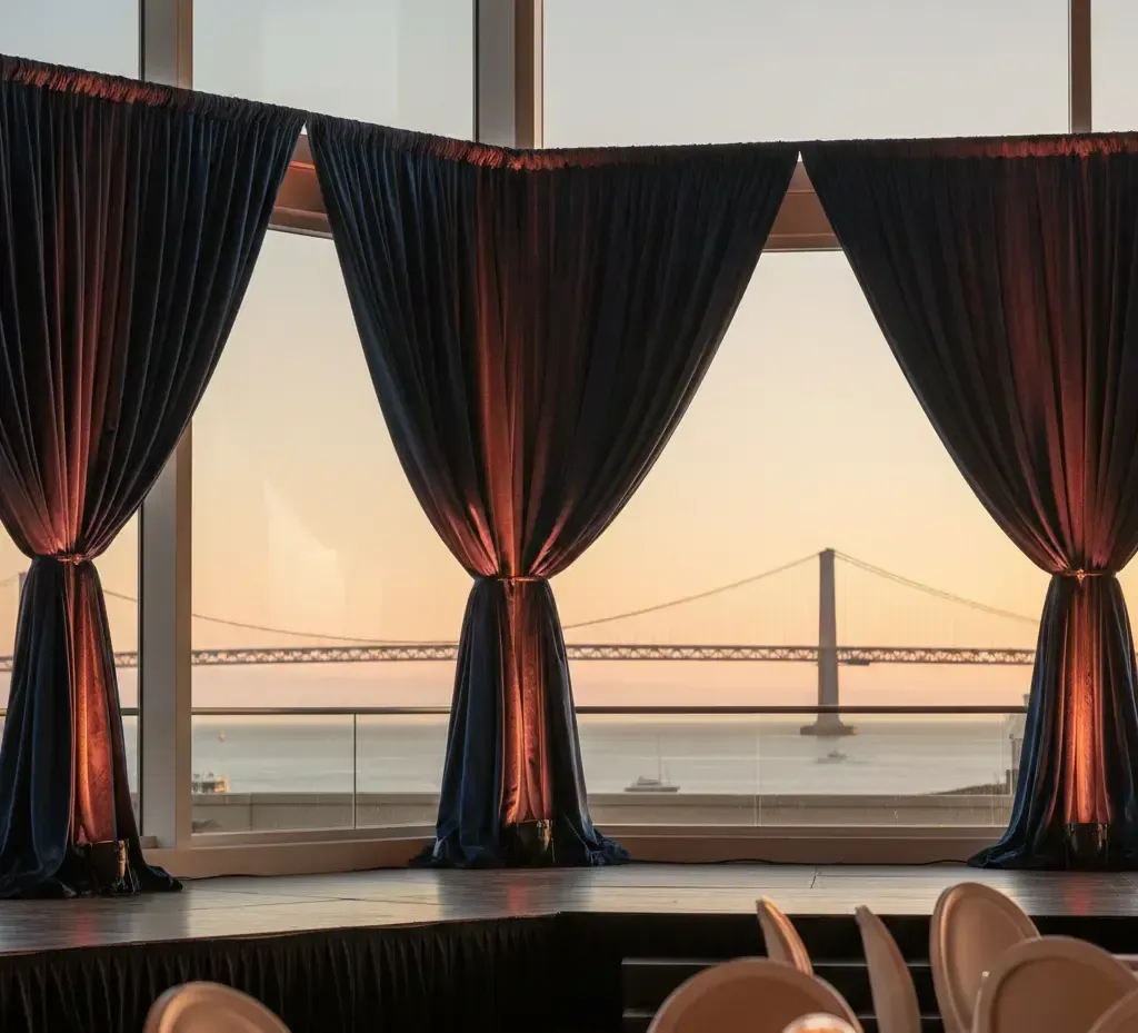 Event backdrop with navy drapes, stage, and bay view with bridge during sunset.