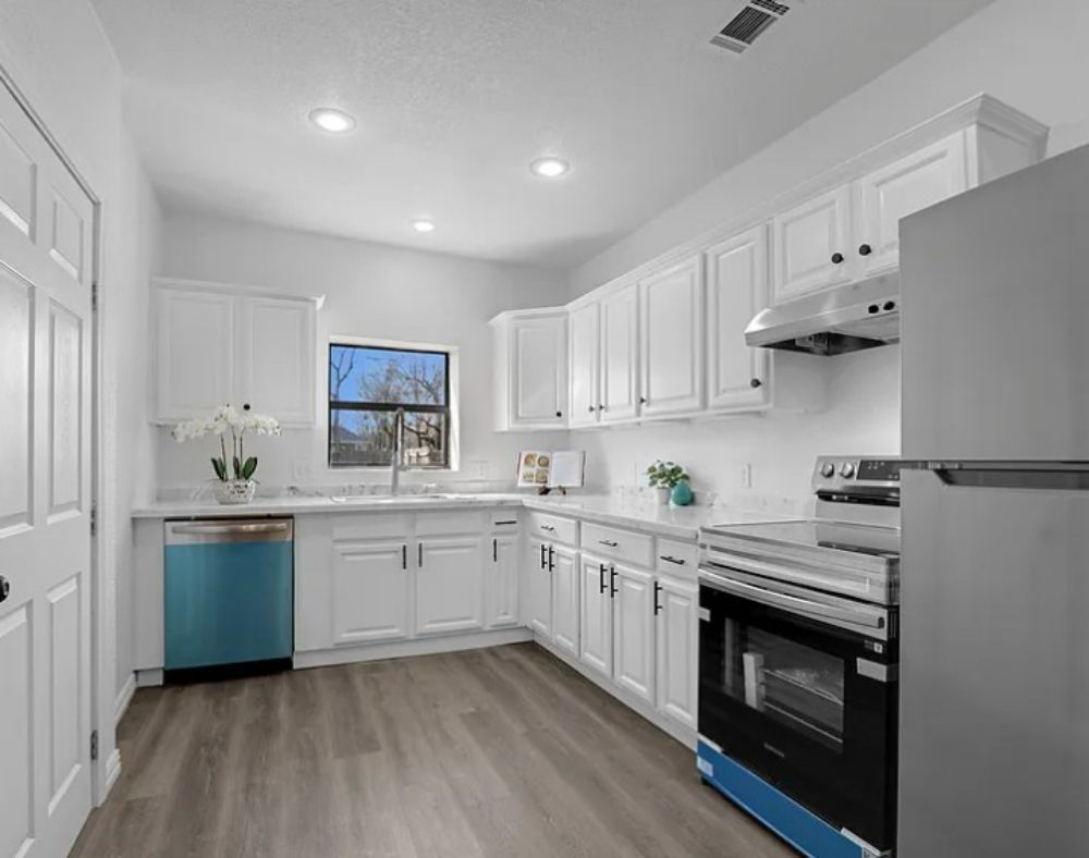 Bright white modern kitchen with blue accents, stainless stove, and wood-look floor