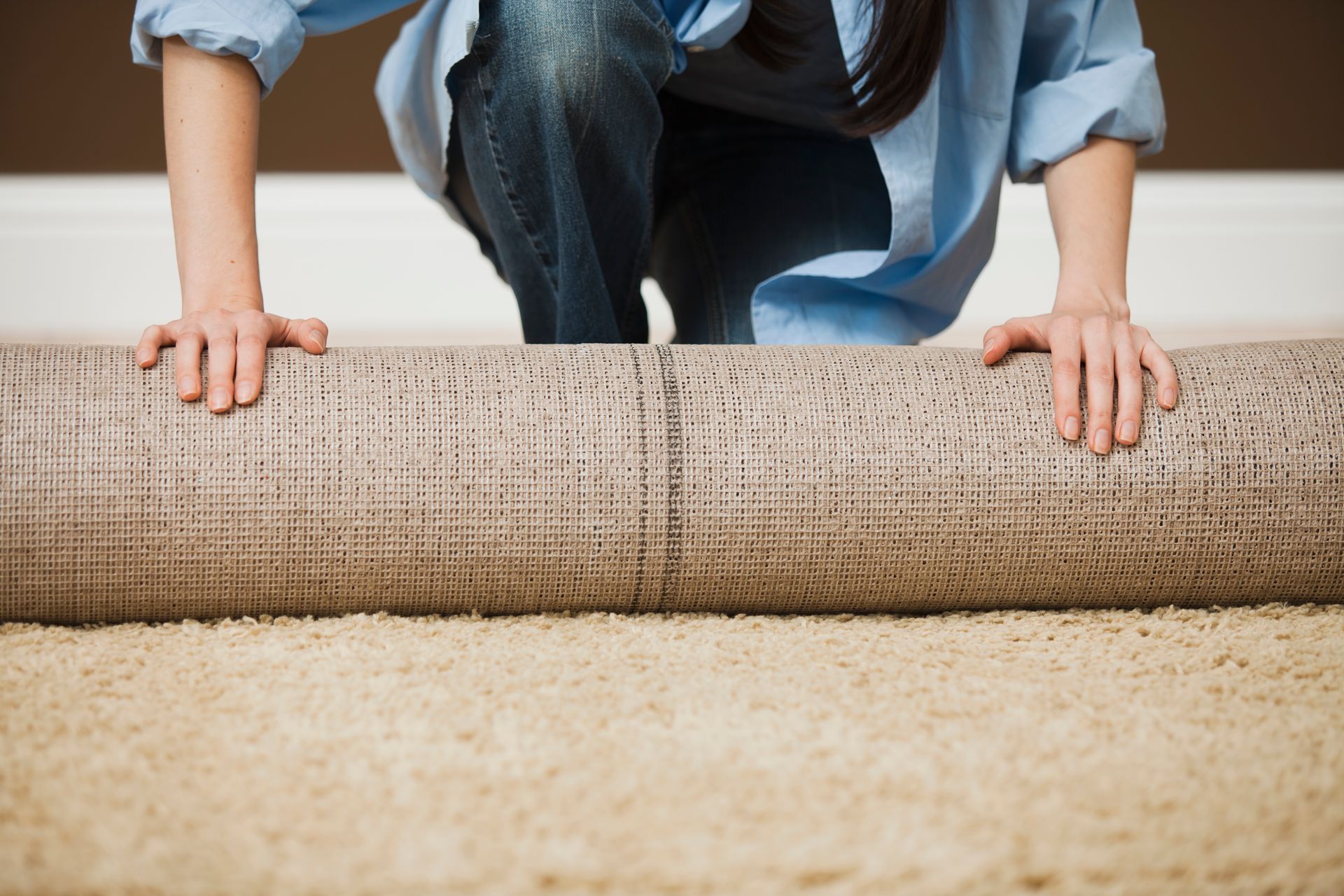 A woman is rolling a rug on the floor.