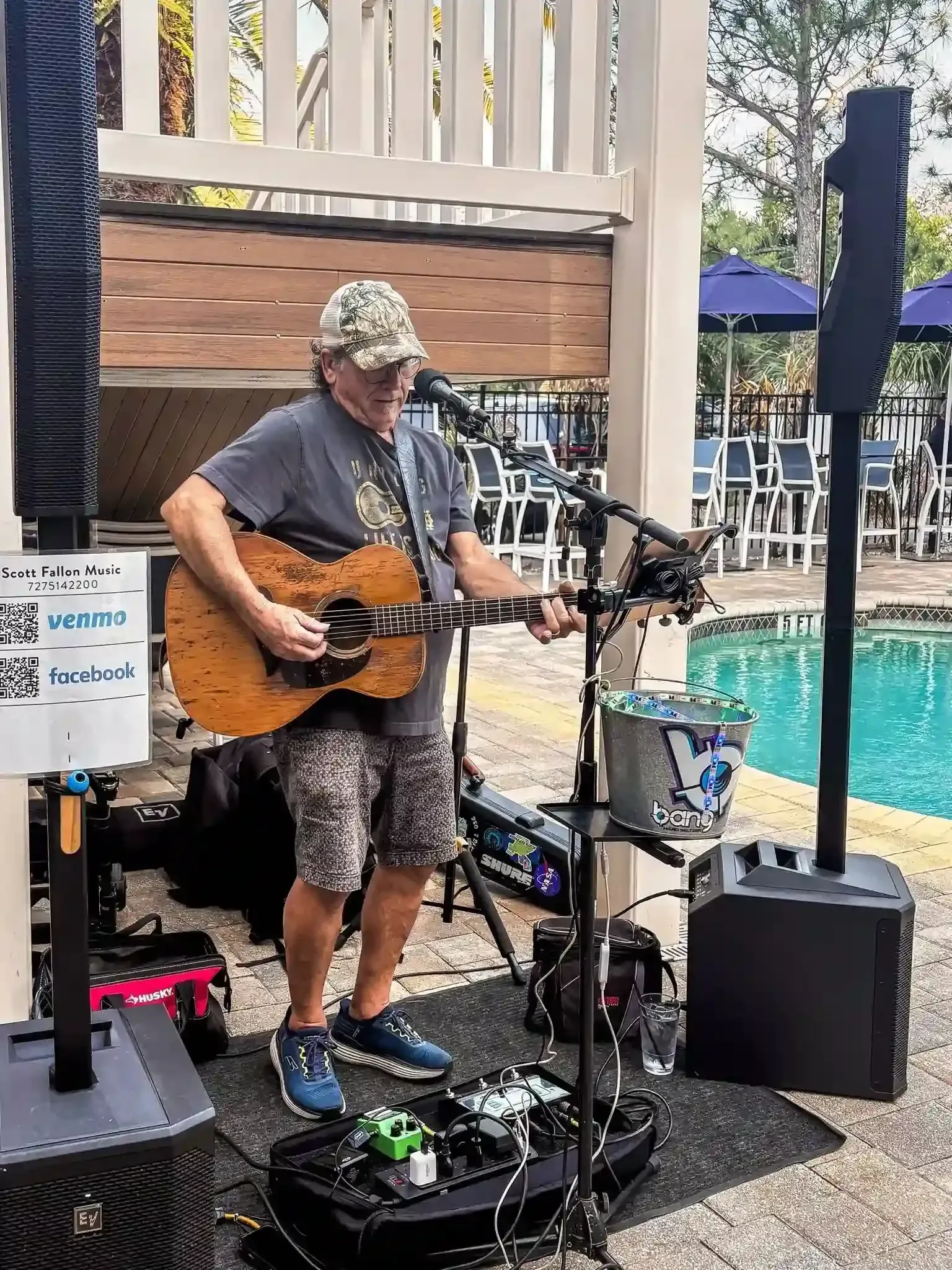 Street musician playing acoustic guitar beside a pool at an outdoor venue