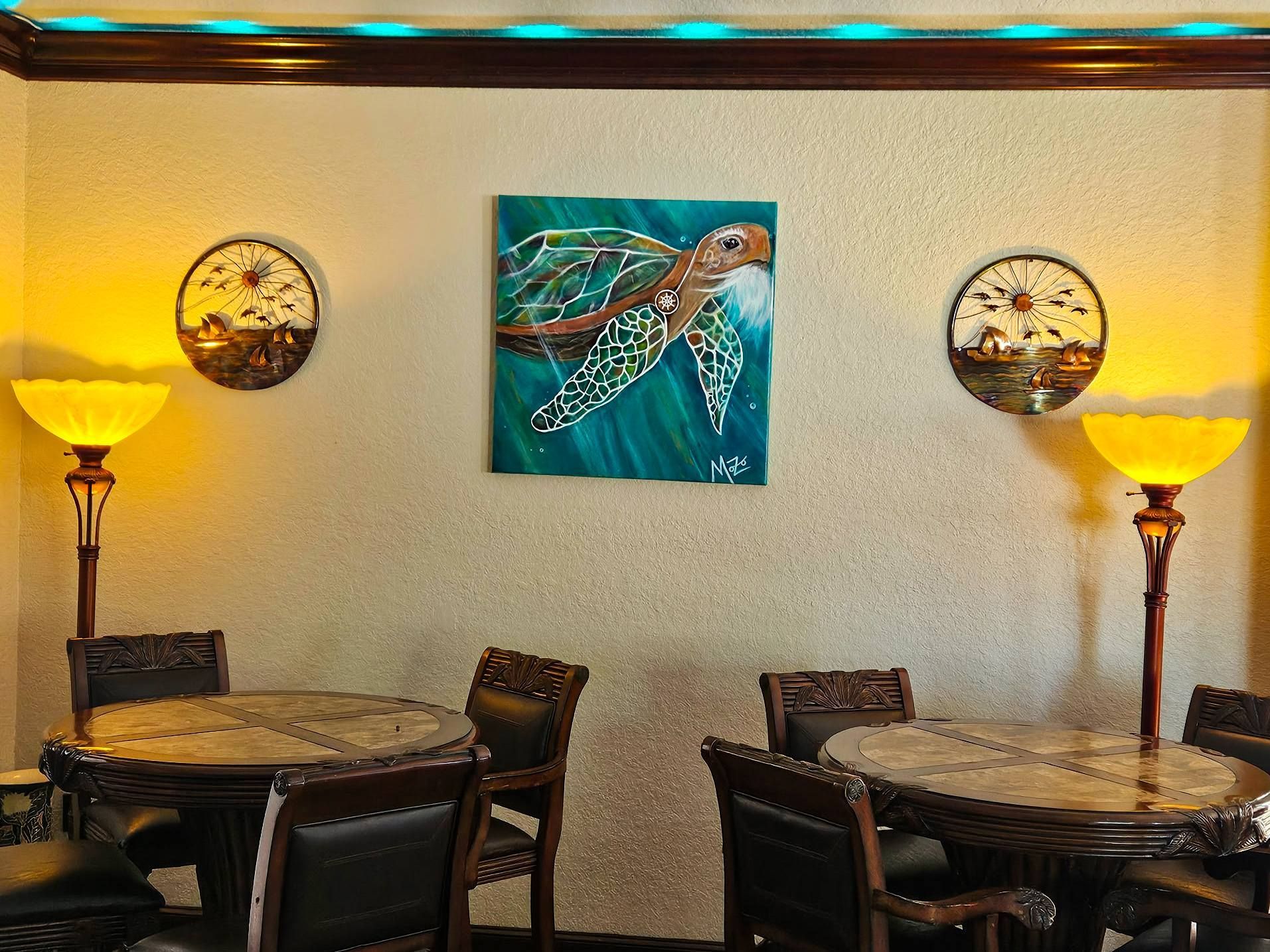 Warm-lit restaurant seating area with round tables, chairs, wall art, and floor lamps