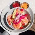 Seafood bowl with shrimp, red onions, avocado, and two dipping sauces on a plate