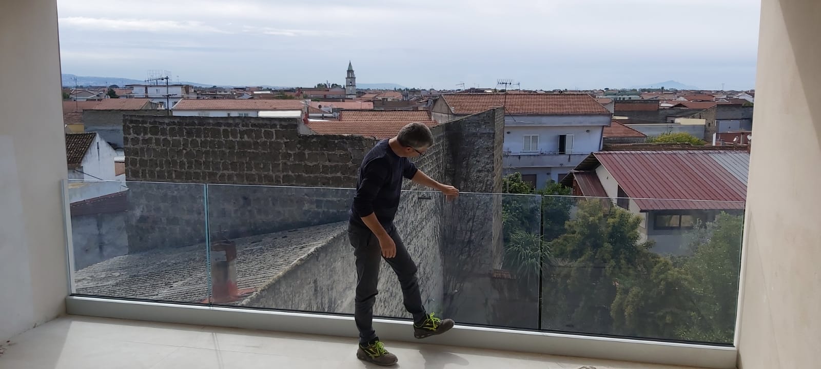 Una persona si trova su un balcone sul tetto, affacciata su un panorama cittadino, appoggiata a una ringhiera di vetro.