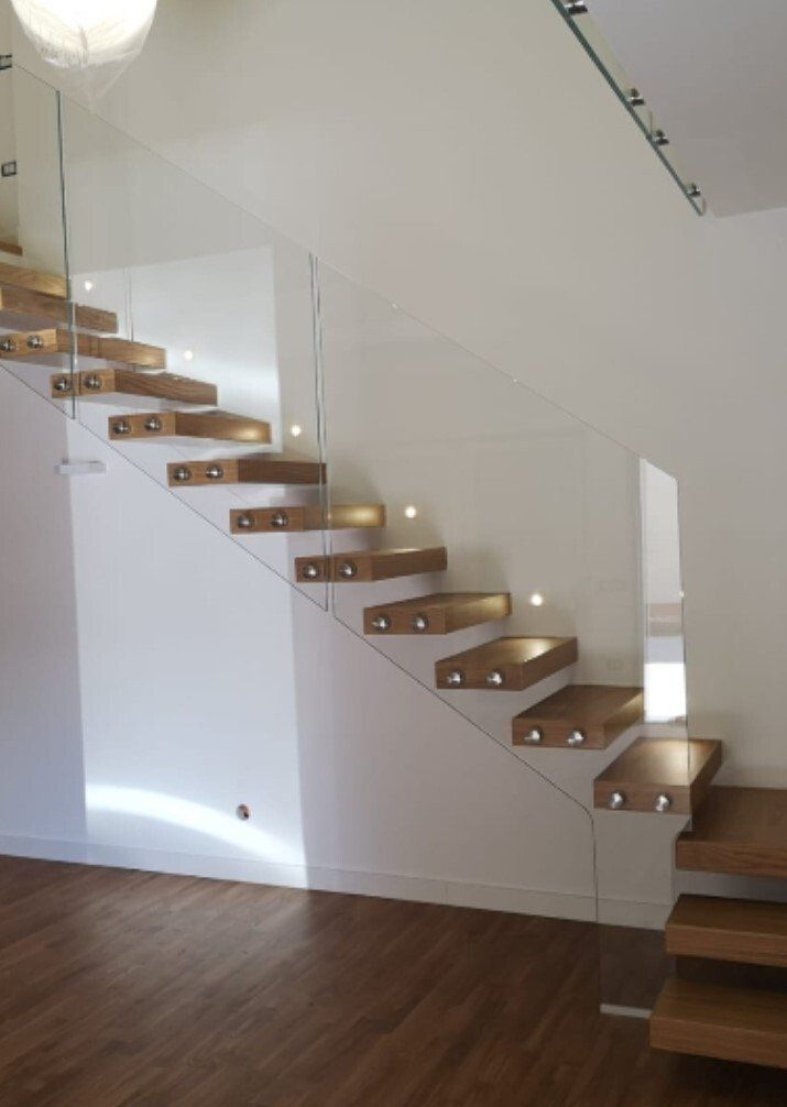 Scala moderna in legno con ringhiera in vetro e luci integrate sui gradini, in un interno bianco.