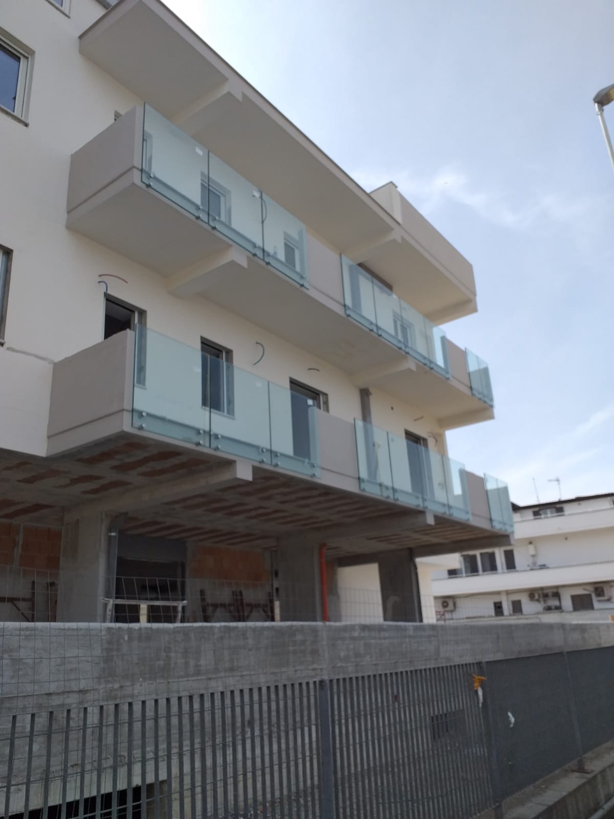 Moderno condominio con balconi in vetro dietro una recinzione di cantiere.
