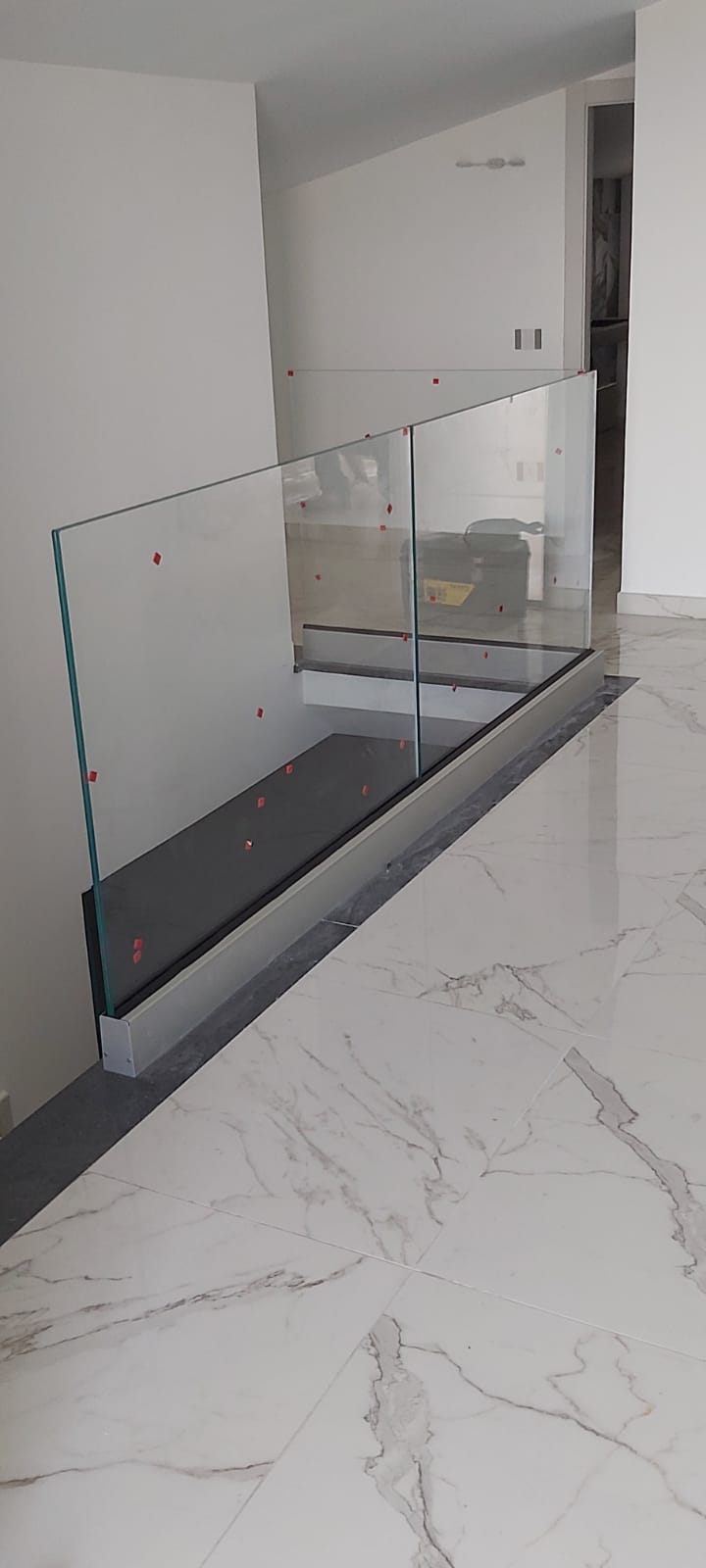 Cucina moderna con ringhiera in vetro accanto a un pavimento effetto marmo bianco e armadi a muro.