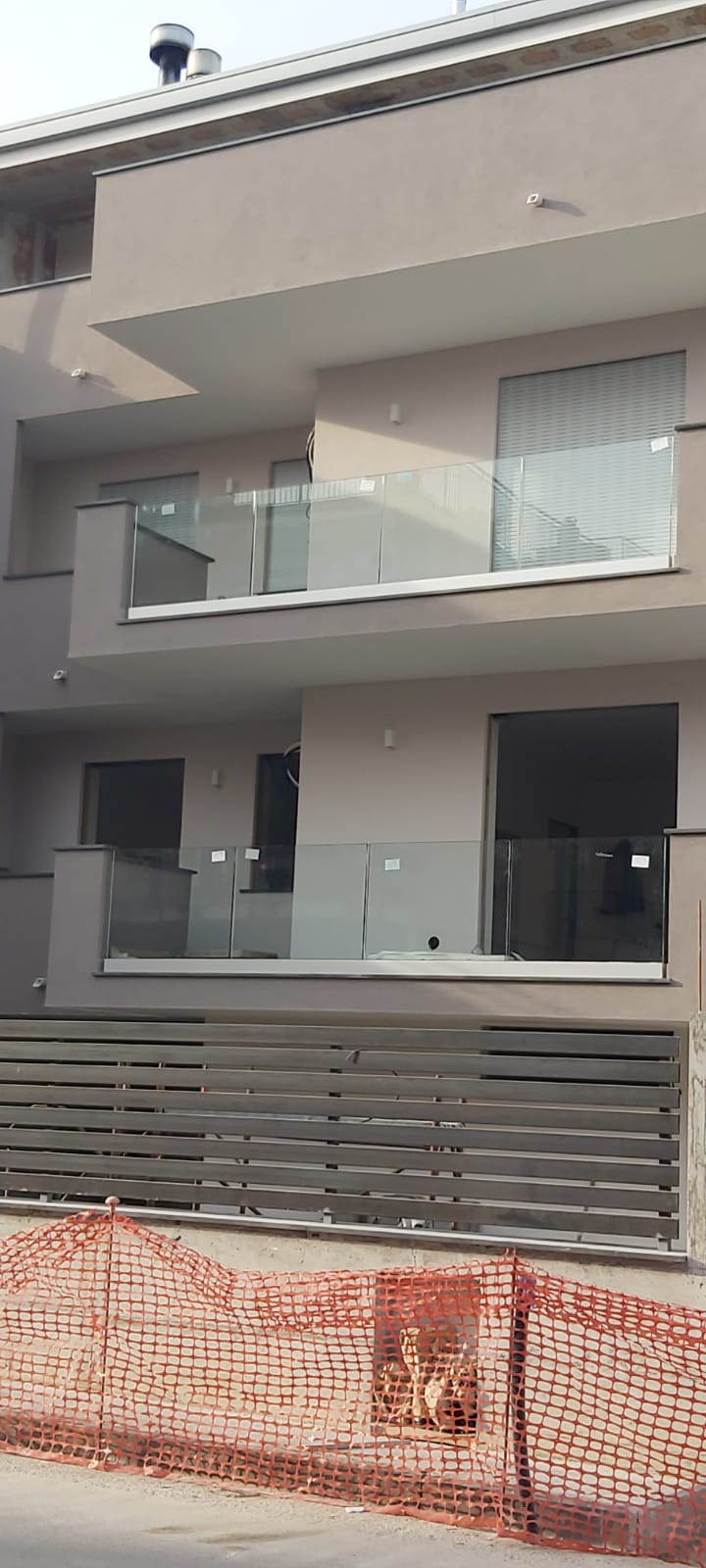 Casa moderna a due piani con balcone, facciata grigia e recinzione a doghe sul davanti.