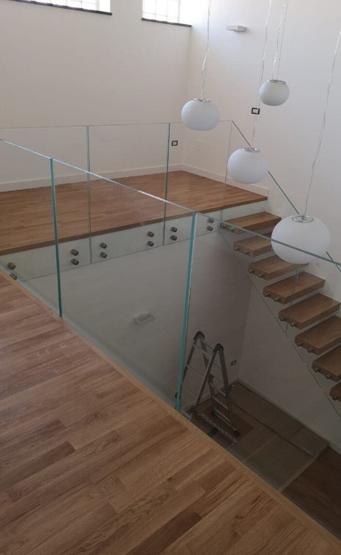 Interni moderni con ringhiera in vetro, scale in legno e lampade a sospensione bianche sopra la tromba delle scale.