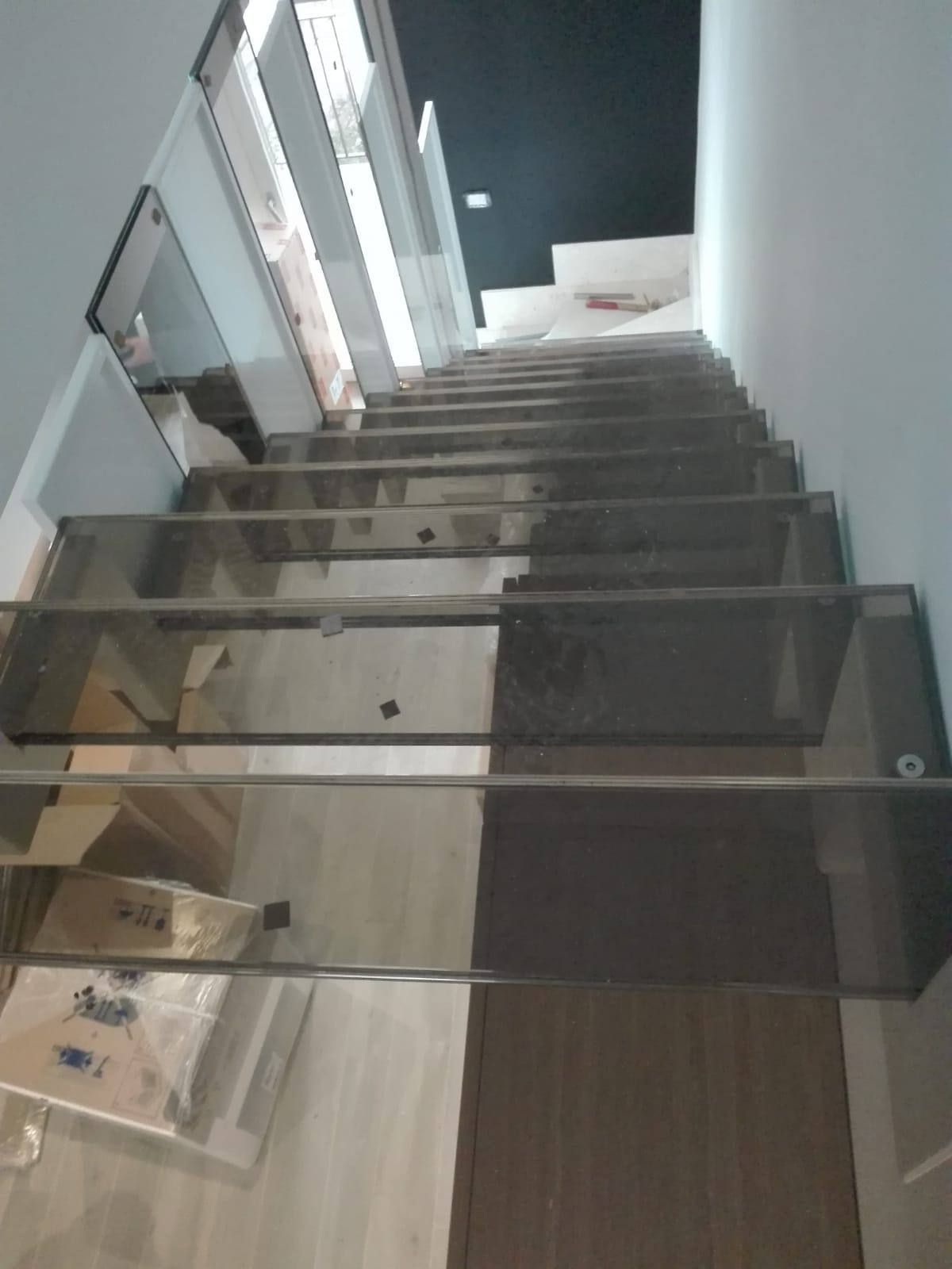 Scala interna con ringhiera in vetro e gradini grigi, vista dal basso verso l'alto.
