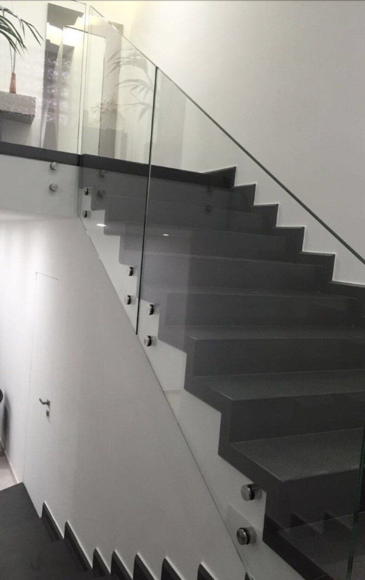 Scala interna moderna con gradini scuri, ringhiera in vetro e pareti bianche.