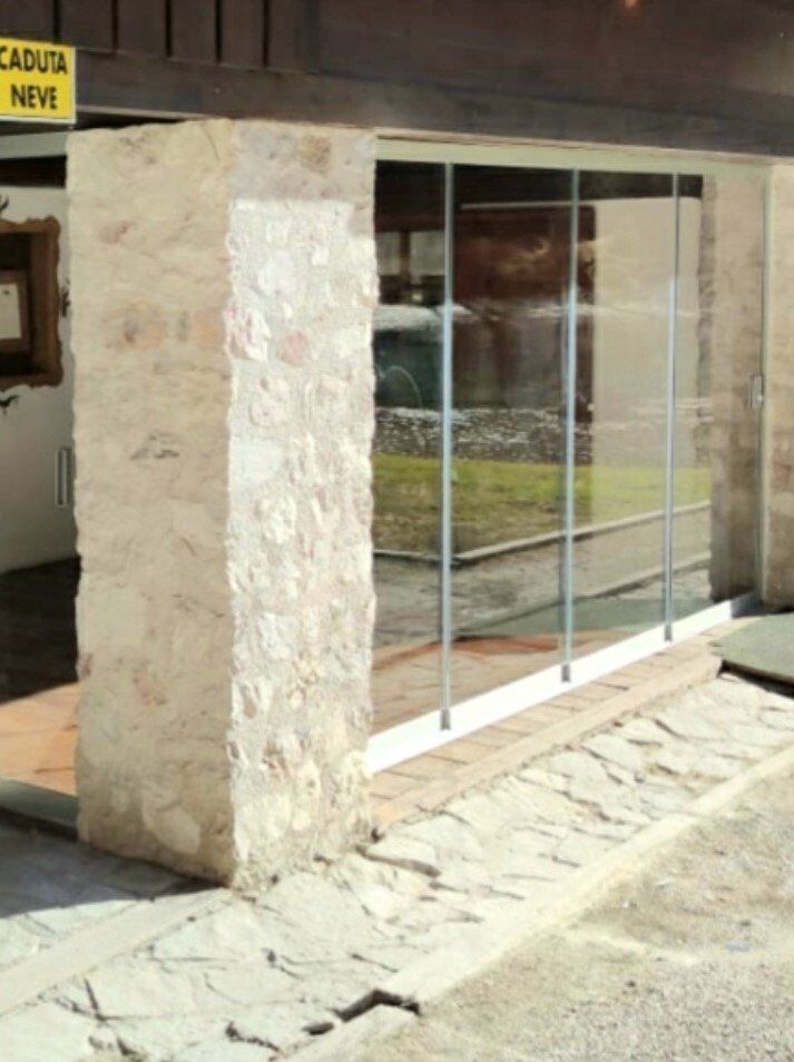 Facciata dell'edificio in pietra con grande porta scorrevole in vetro e marciapiede crepato antistante.