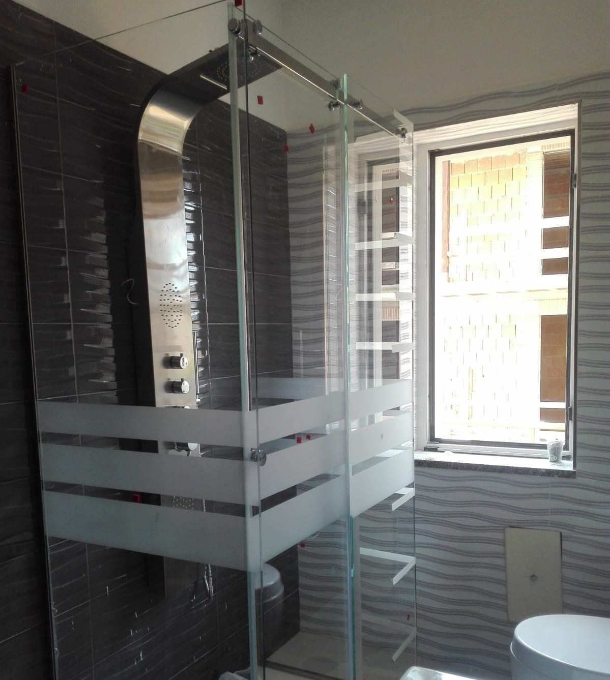 Bagno moderno con box doccia in vetro, WC e porta che si apre su un luminoso balcone.