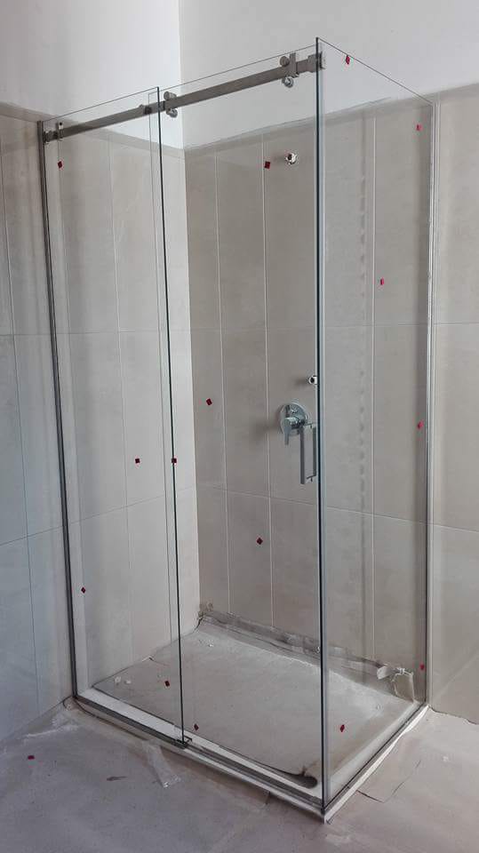 Box doccia in vetro con porta scorrevole e telaio in metallo in un bagno piastrellato.