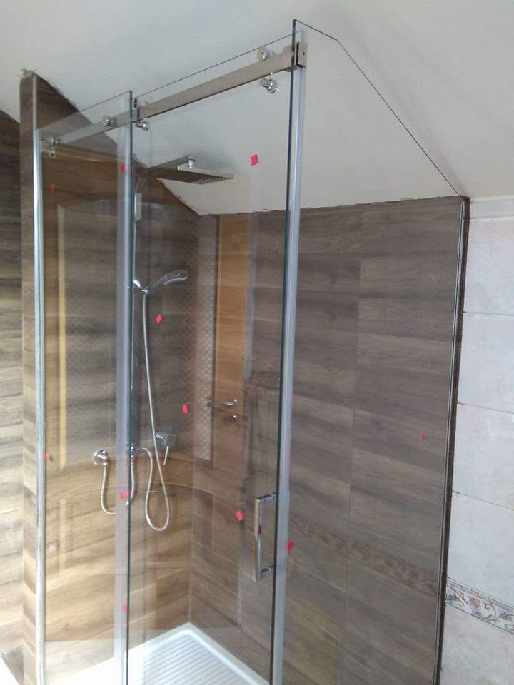 Box doccia in vetro con telaio cromato e pareti rivestite con piastrelle effetto legno in un bagno moderno.