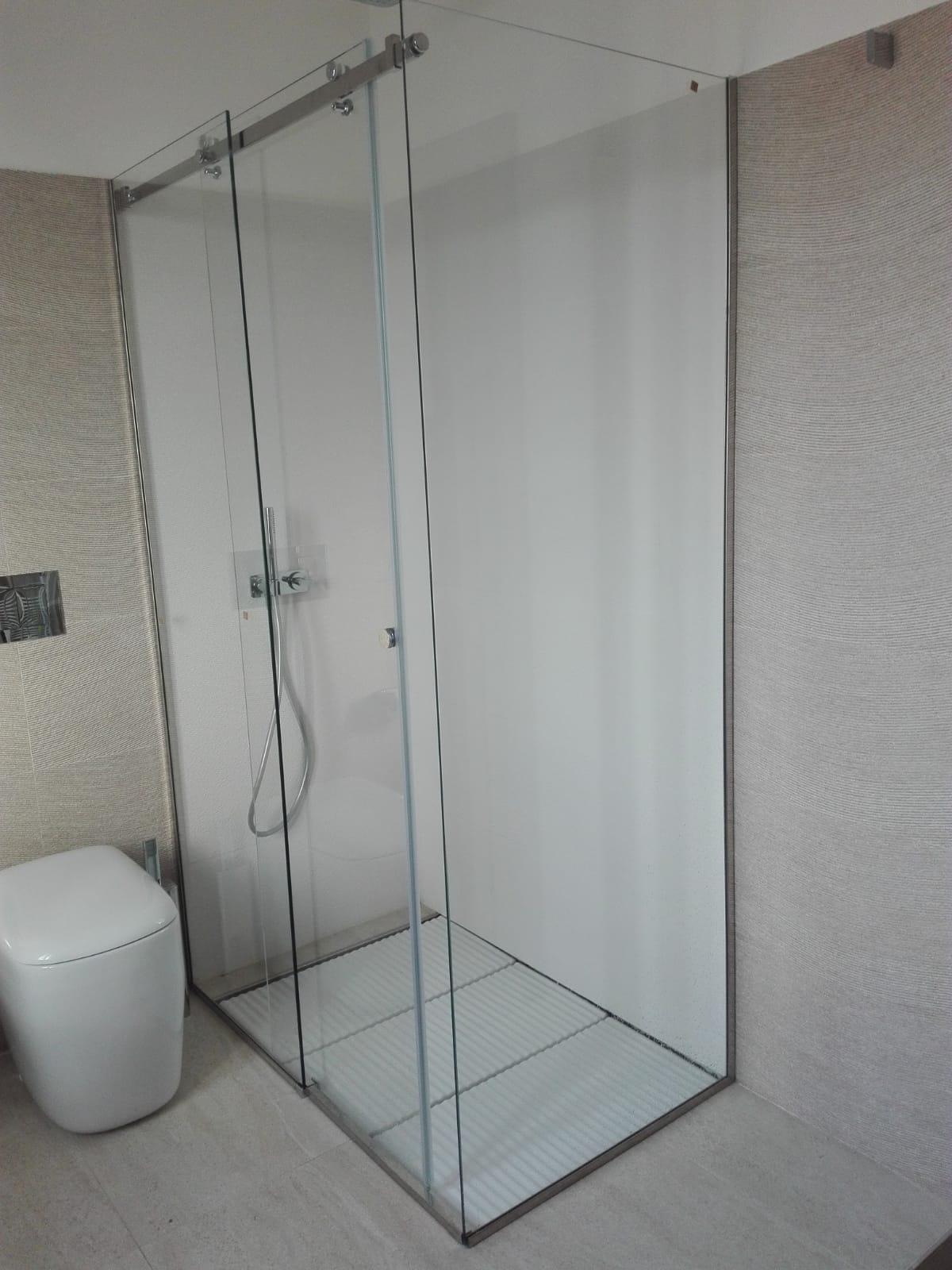 Box doccia in vetro in un bagno piastrellato con WC bianco nelle vicinanze.
