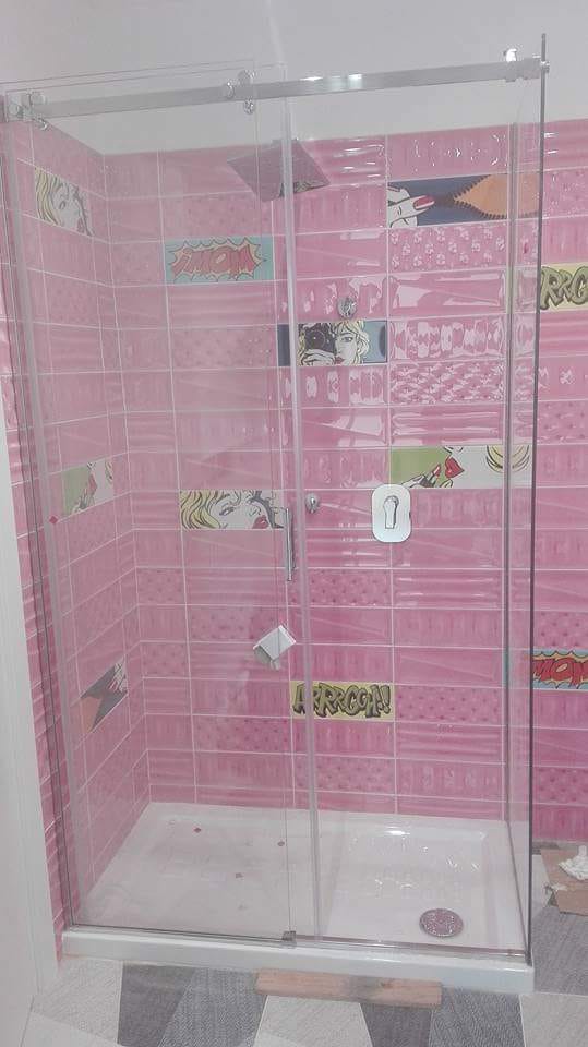Doccia del bagno rivestita di piastrelle rosa con box doccia in vetro trasparente e piatto doccia bianco.