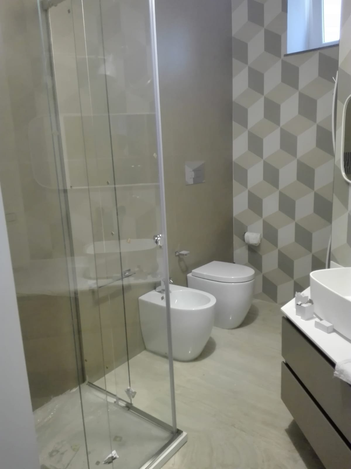 Bagno moderno con doccia in vetro, bidet e WC bianchi e parete decorativa con piastrelle decorate.
