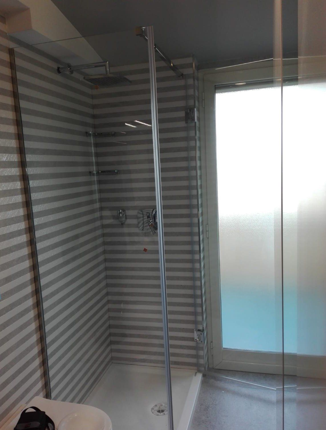 Bagno moderno con box doccia in vetro a righe, pavimento blu e finestra satinata.