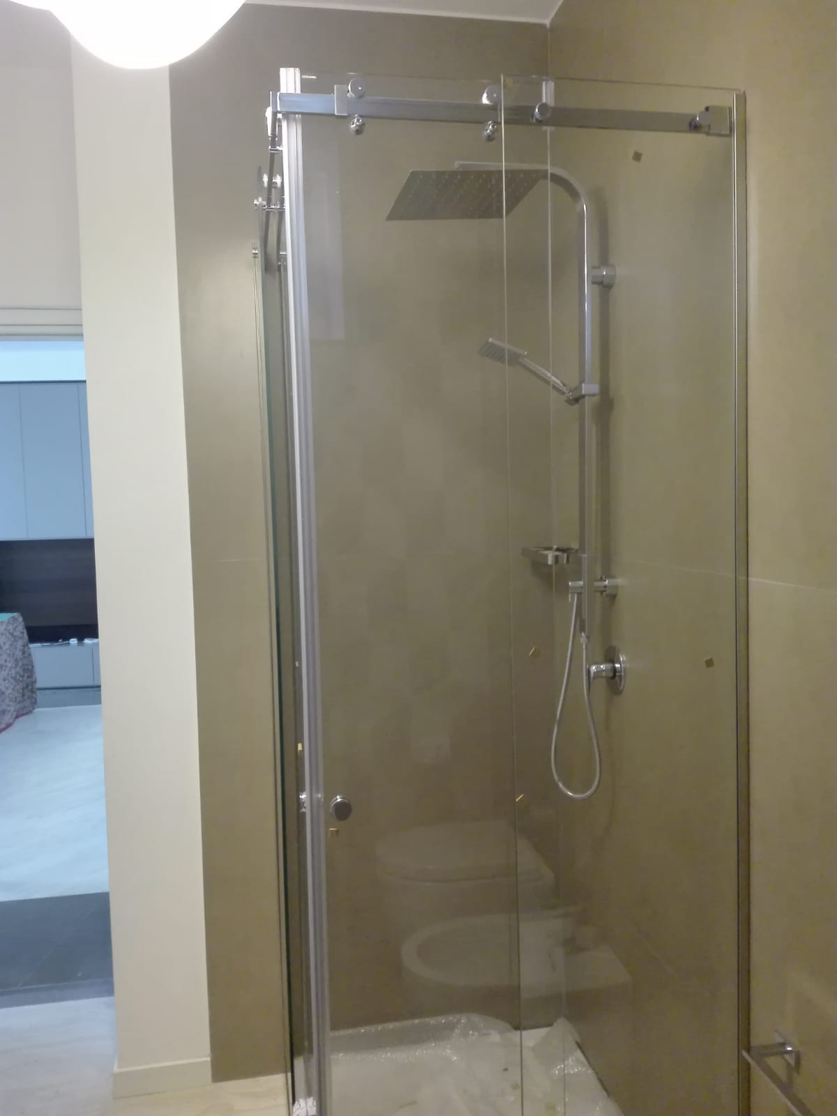 Cabina doccia in vetro con rubinetteria cromata e pareti rivestite con piastrelle beige.