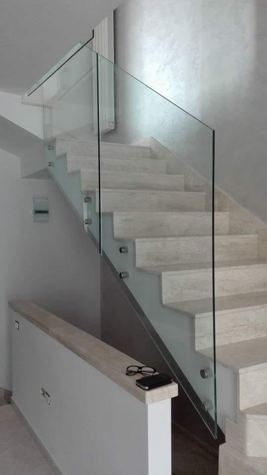 Scala moderna con ringhiera in vetro e gradini in marmo bianco in un interno luminoso.