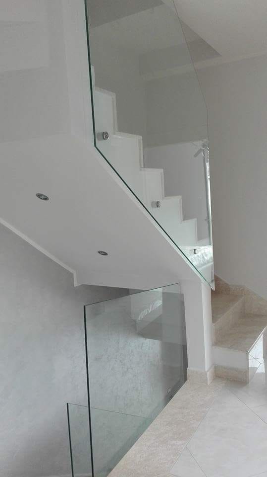 Scala interna moderna con ringhiera in vetro e gradini rivestiti in moquette chiara in un corridoio luminoso e minimalista.