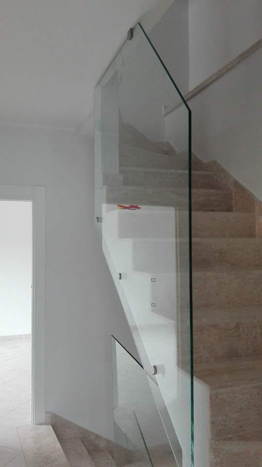 Ringhiera in vetro accanto a gradini rivestiti di moquette in un corridoio bianco e luminoso.