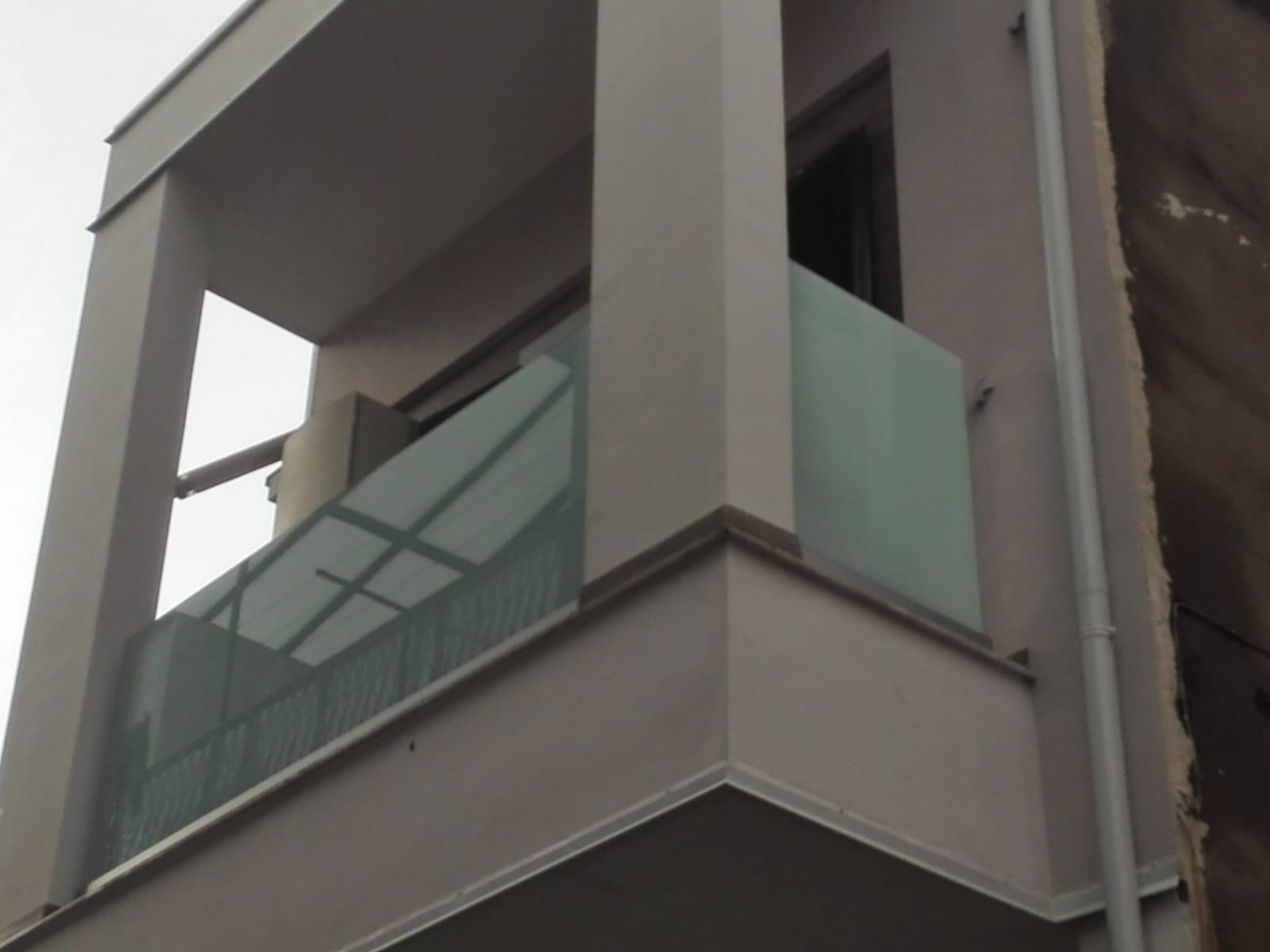 Balcone di un appartamento moderno con ringhiere in vetro satinato e pareti esterne grigie.