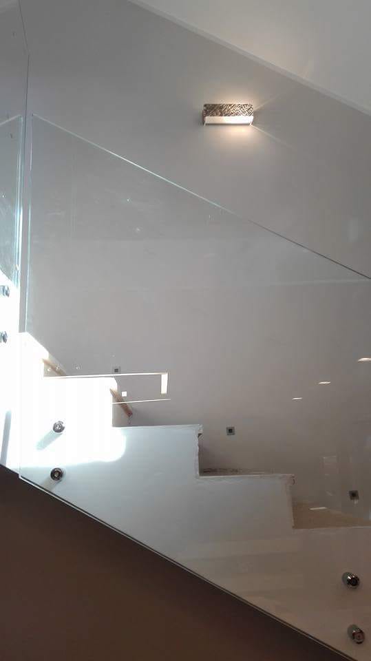 Scala moderna con pareti bianche, ringhiera in vetro e applique in un interno minimalista