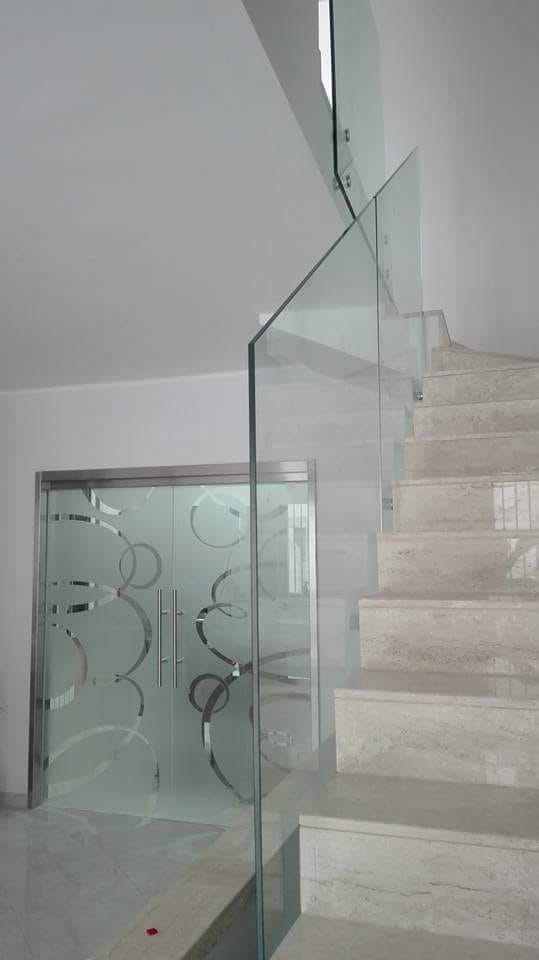 Scala con ringhiera in vetro e gradini in marmo bianco, adiacente a una parete in vetro satinato con pannello decorativo.