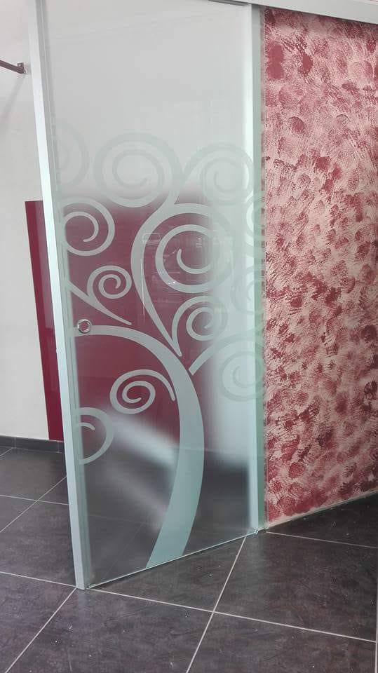 Porta decorativa in vetro satinato con motivi a spirale bianchi in un corridoio piastrellato.