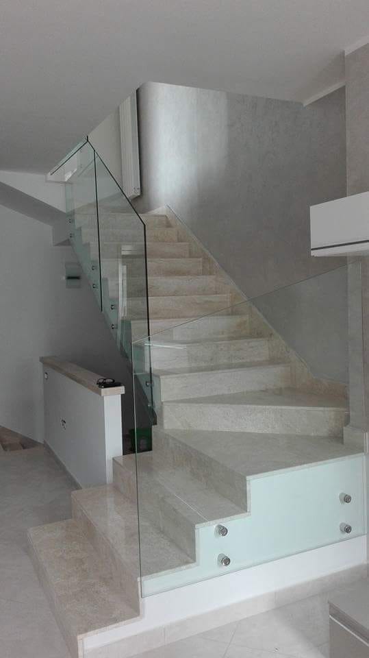 Scala interna moderna con ringhiera in vetro e gradini beige in una casa luminosa.