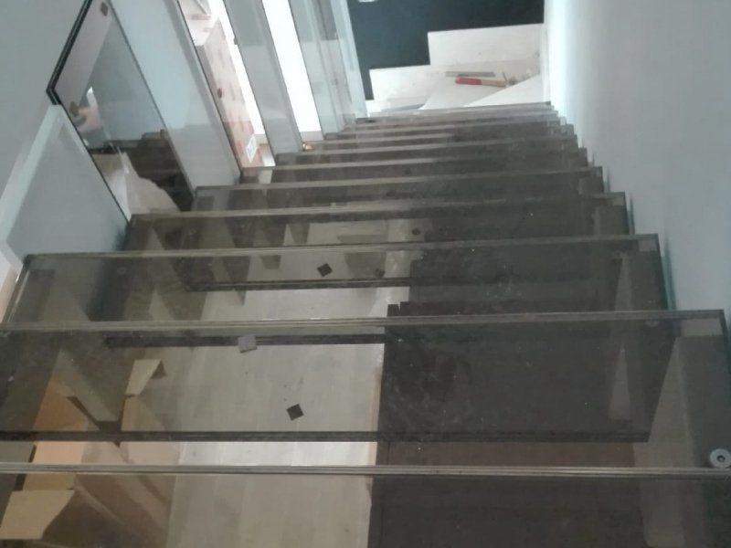 Scala interna con ringhiera in vetro e pareti grigie, vista dall'alto.